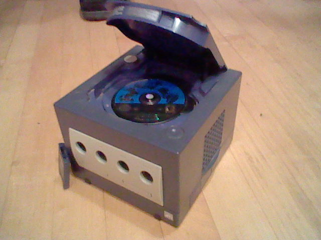 Photo of a Gamecube with the disk drive open and the memory card sitting next to it.