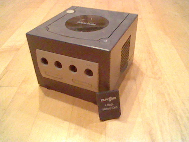 Photo of a Gamecube with the memory card leaning  on it.